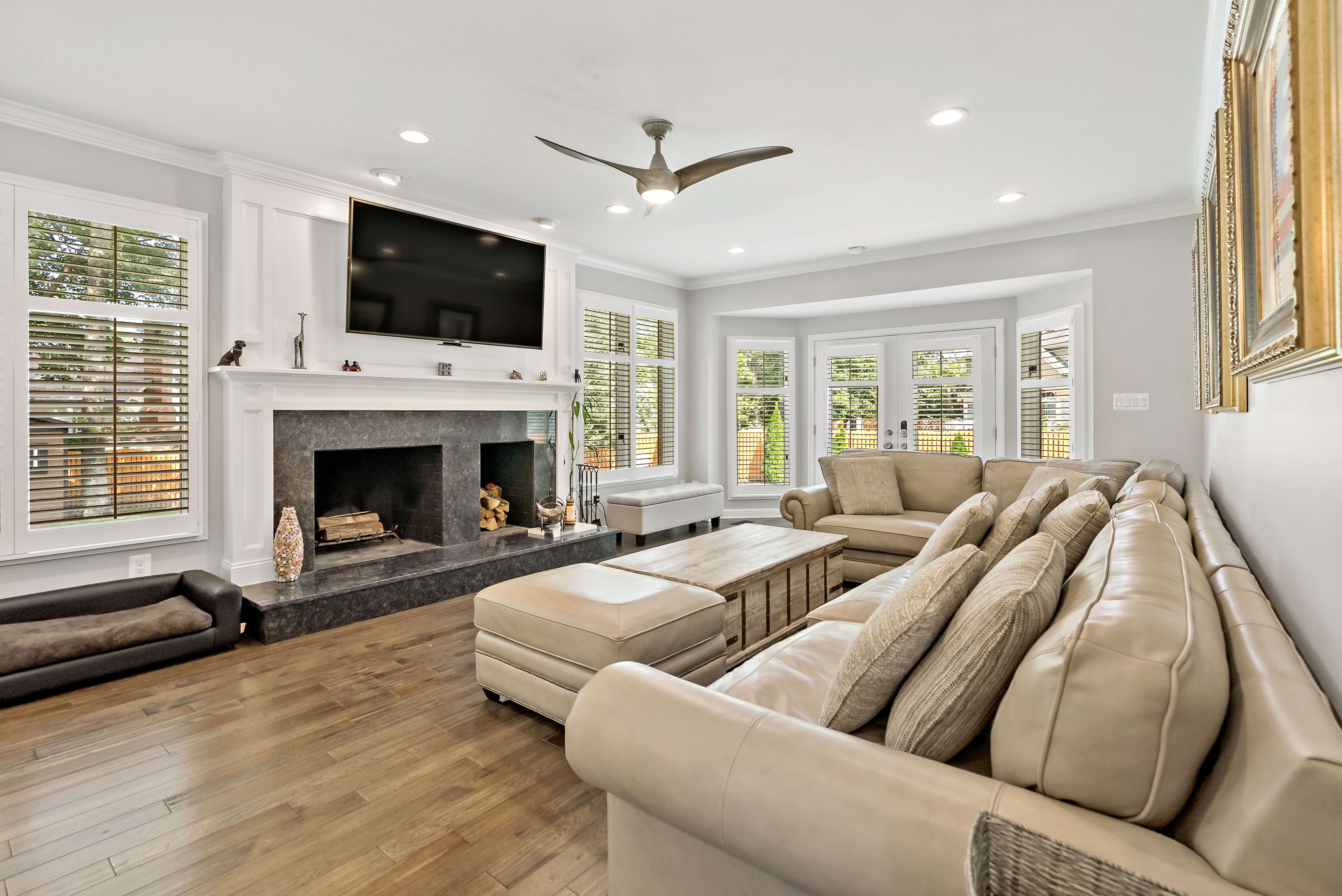 Living room with fireplace, mantle, mounted tv with lots or windows and large couch