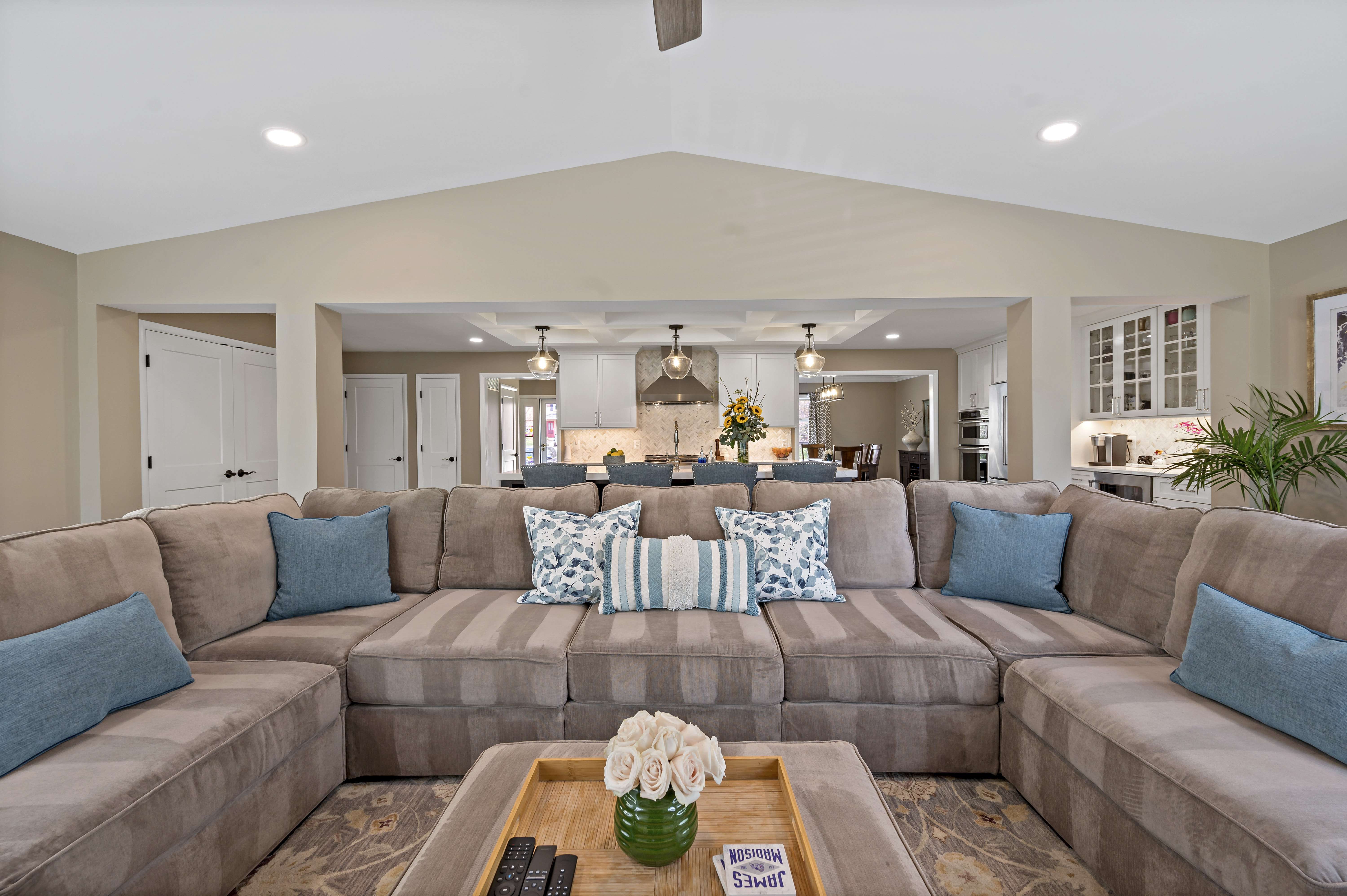 Brown sectional couch in living room with cathedral ceiling and open kitchen in back