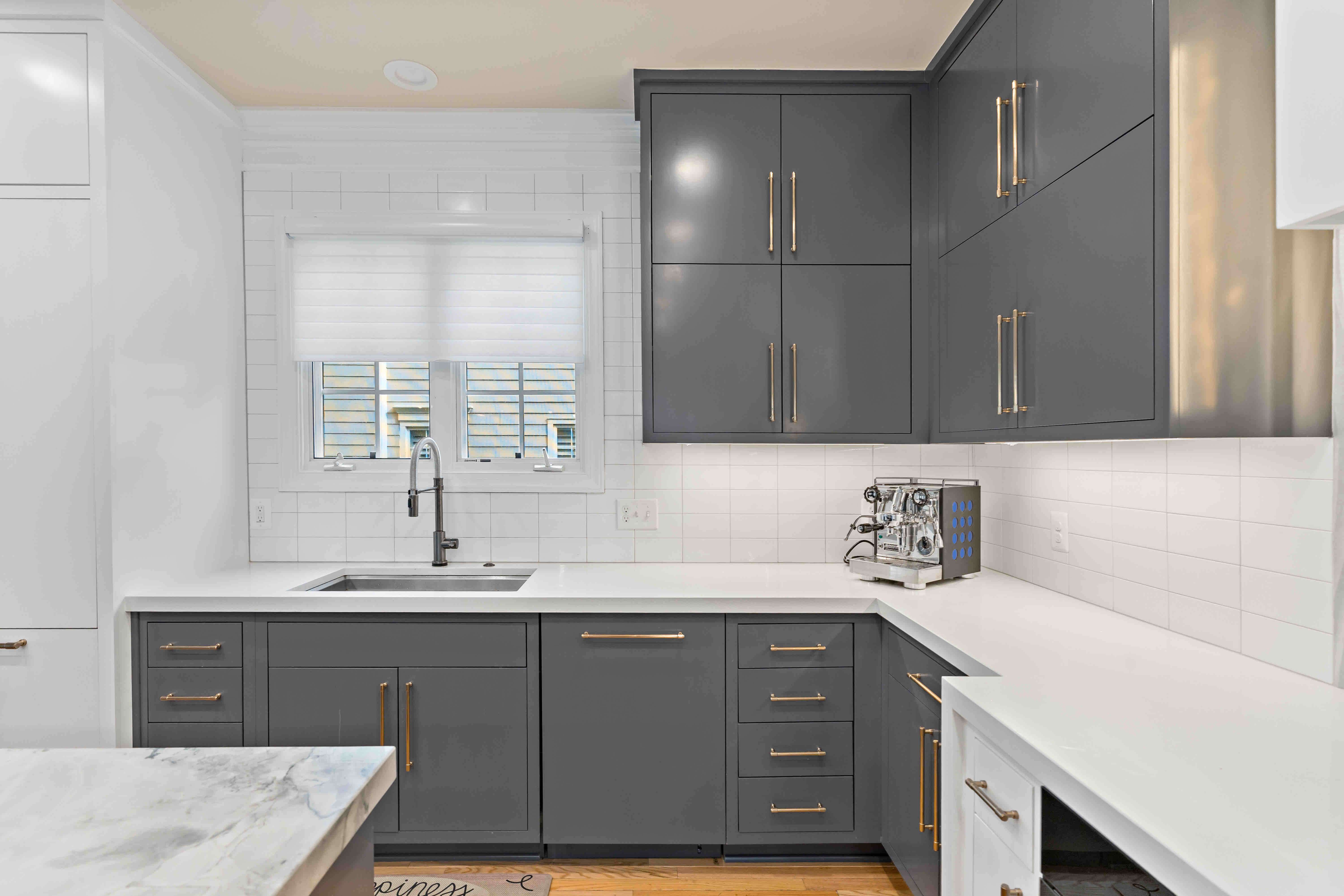 White countertop and backsplash in kitchen with grey cabinets and gold fixtures