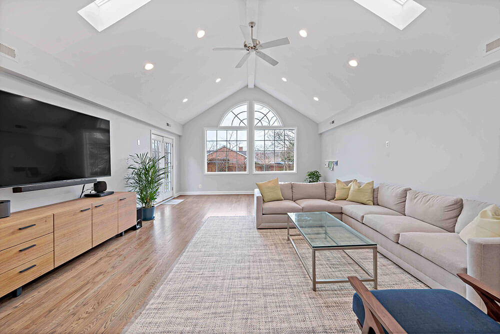 Spacious family room with large pink couch and cathedral ceiling with accent window
